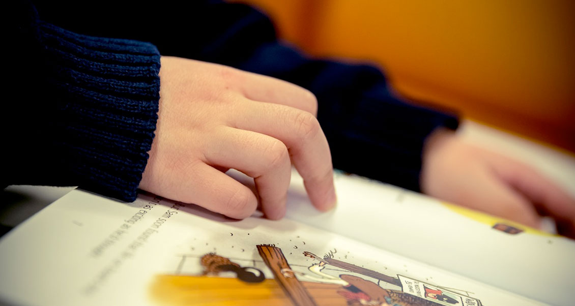 Hand of a child pointing to a line on a book. 