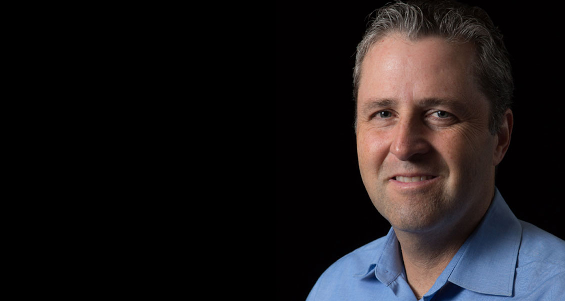 Dr. Hernandez smiling at camera, dark background. 