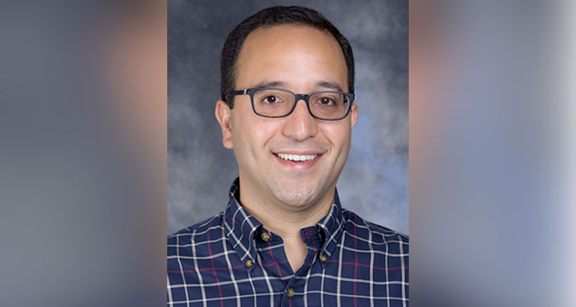 Dr. Viana looking at the camera smiling, grayish background. 