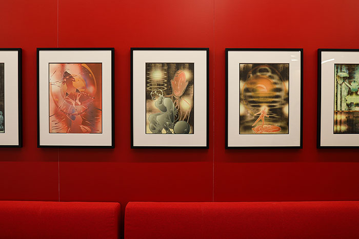 Front view of a collection of framed digital photographs on a red wall above red lounge seating