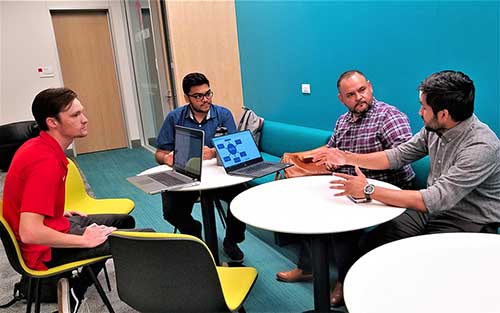 Four people in a discussion sit a round tables in a lounge.