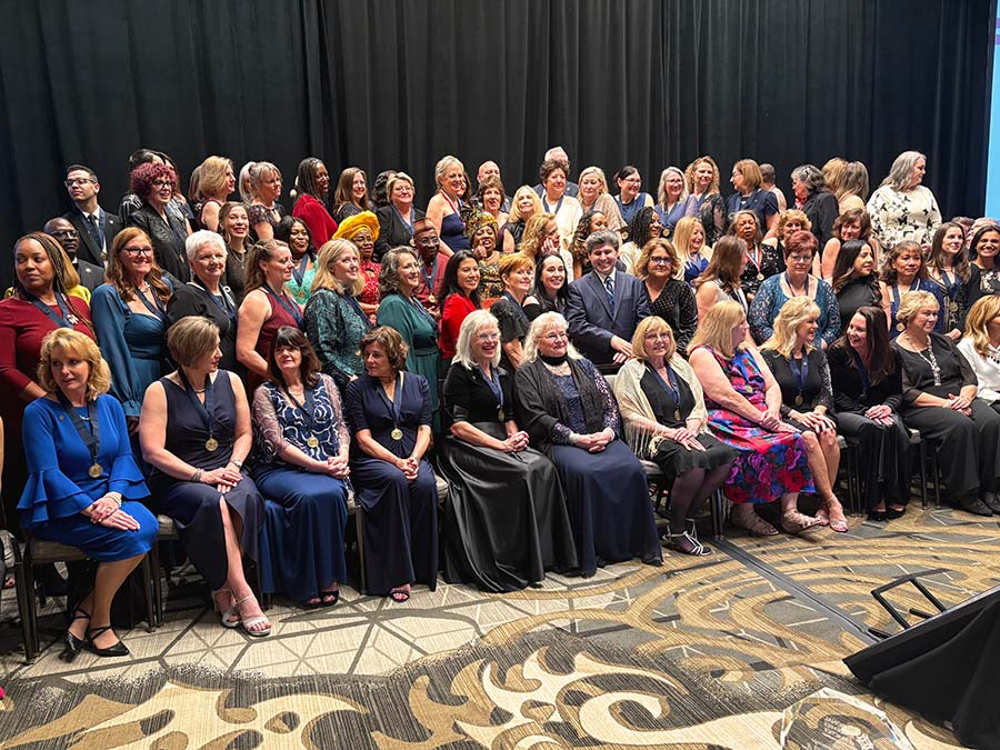 Dozens of women in formal evening wear sit and stand together for a photograph