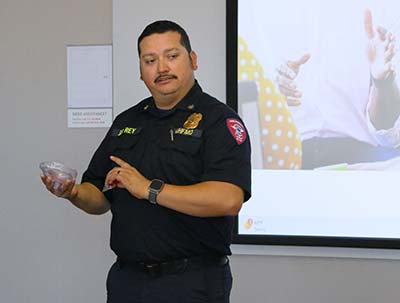 A Hispanic man stands in front of a projection screen a points to a transparent CPR oxygen mask with a value.